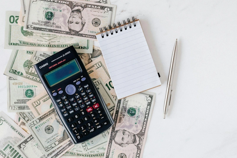 calculator, notes and pen on top of a dollar representing cost and budget for marketing