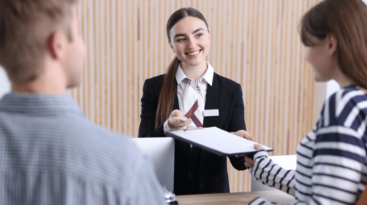 Hotel receptionist check in guests front desk A receptionist at a motel front desk assisting a couple with check-in paperwork to illustrating effective motel SEO sfra.