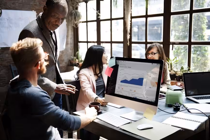 A diverse team discussing small business growth and operational data on a computer screen in a bright office.