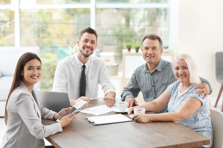 A male and female professional sit at a table with a laptop and tablet while consulting a mature couple, showcasing SEO for insurance agents.